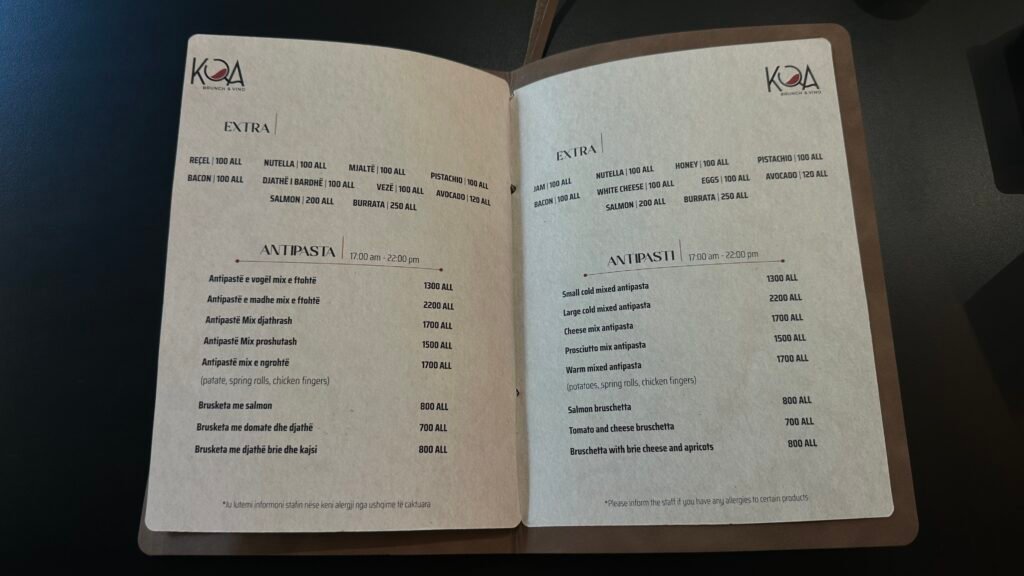 Image 1: EXTRA & ANTIPASTA Sections
Albanian (Left Side):
EXTRA:
REFEL | 100 ALL
BACON | 100 ALL
DJATHE I BARDHE | 100 ALL
VEZË | 100 ALL
MJALTË | 100 ALL
PISTACHIO | 100 ALL
AVOCADO | 120 ALL
SALMON | 200 ALL
BURRATA | 250 ALL
ANTIPASTA | 17:00 am - 22:00 pm:
Antipastë e vogel mix e ftohtë | 1300 ALL
Antipastë e madhe mix e ftohtë | 2200 ALL
Antipastë Mix djathrash | 1700 ALL
Antipastë Mix proshutash | 1500 ALL
Antipastë mix e ngrohtë (patate, spring rolls, chicken fingers) | 1700 ALL
Brusketa me salmon | 800 ALL
Brusketa me domate dhe djathe | 700 ALL
Brusketa me djathe brie dhe kajsi | 800 ALL
*Ju lutemi informoni stafin nëse keni alergi nga ushqimet të caktuara
English (Right Side):
EXTRA:
JAM | 100 ALL
NUTELLA | 100 ALL
WHITE CHEESE | 100 ALL
SALMON | 200 ALL
BACON | 100 ALL
EGGS | 100 ALL
HONEY | 100 ALL
PISTACHIO | 100 ALL
AVOCADO | 120 ALL
BURRATA | 250 ALL
ANTIPASTI | 17:00 am - 22:00 pm:
Small cold mixed antipasta | 1300 ALL
Large cold mixed antipasta | 2200 ALL
Cheese mix antipasta | 1700 ALL
Prosciutto mix antipasta | 1500 ALL
Warm mixed antipasta (potatoes, spring rolls, chicken fingers) | 1700 ALL
Salmon bruschetta | 800 ALL
Tomato and cheese bruschetta | 700 ALL
Bruschetta with brie cheese and apricots | 800 ALL
*Please inform the staff if you have any allergies to certain products